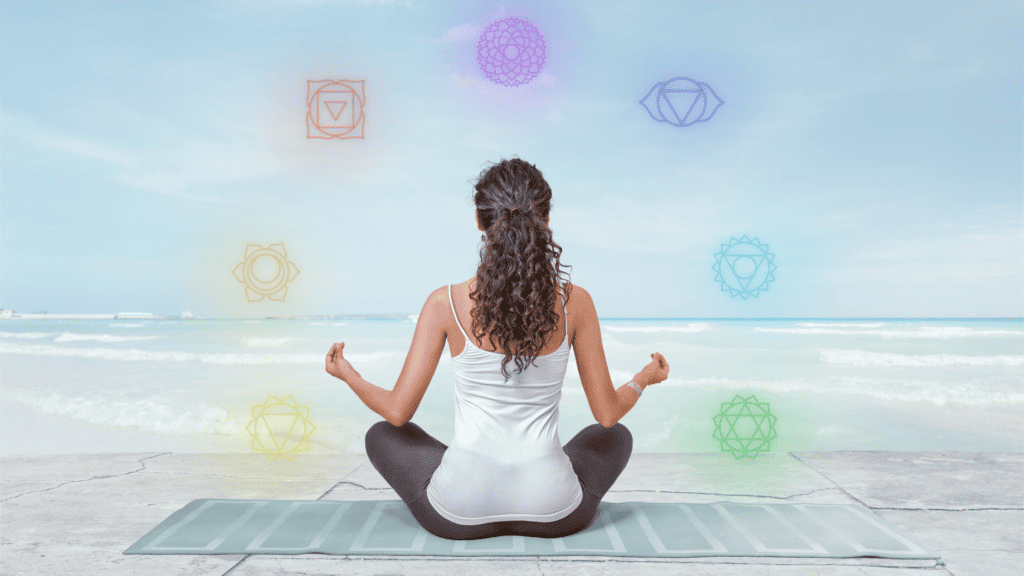 Woman meditating on the beach with chakra symbols for healing and energy alignment.