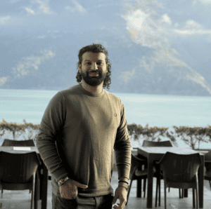 Psychic Medium Daksh standing outdoors with lake and mountains in background.